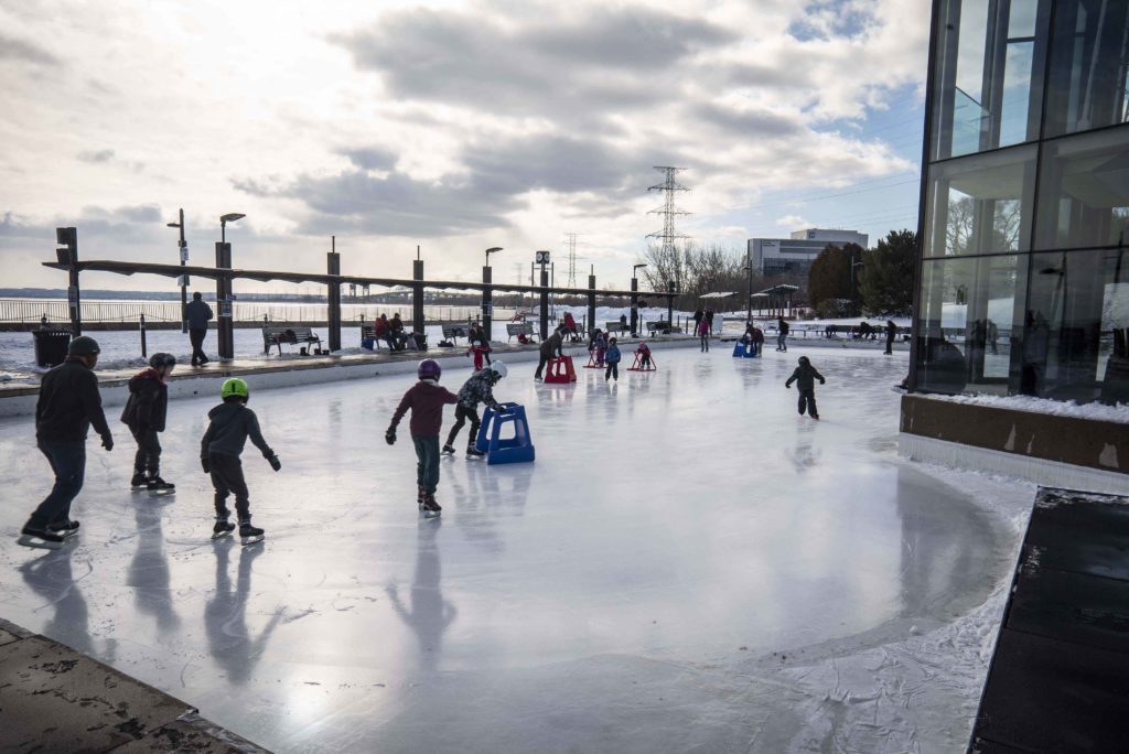 Skaters on Rotary Centennial Pond in Spencer Smith Park with skyway in background