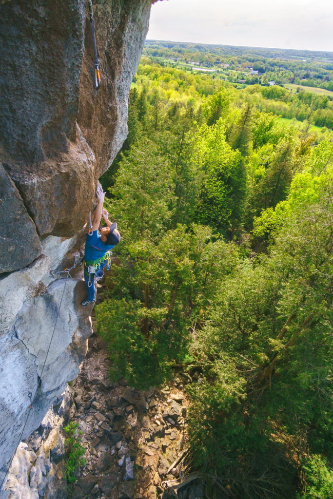 Rock Climbing - man holding onto rock with trees below him